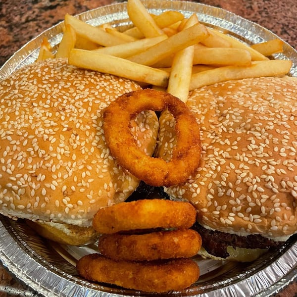 Two burgers with sesame seed buns, fries, and onion rings in a foil container from Offshore Diner.