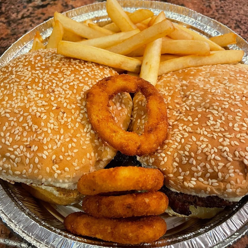 Two burgers with sesame seed buns, fries, and onion rings in a foil container from Offshore Diner.