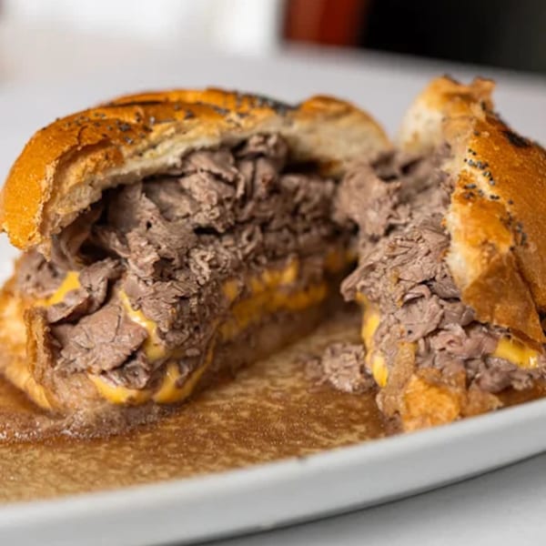 A sliced French dip sandwich with roast beef and melted cheese, soaking in au jus on a white plate.