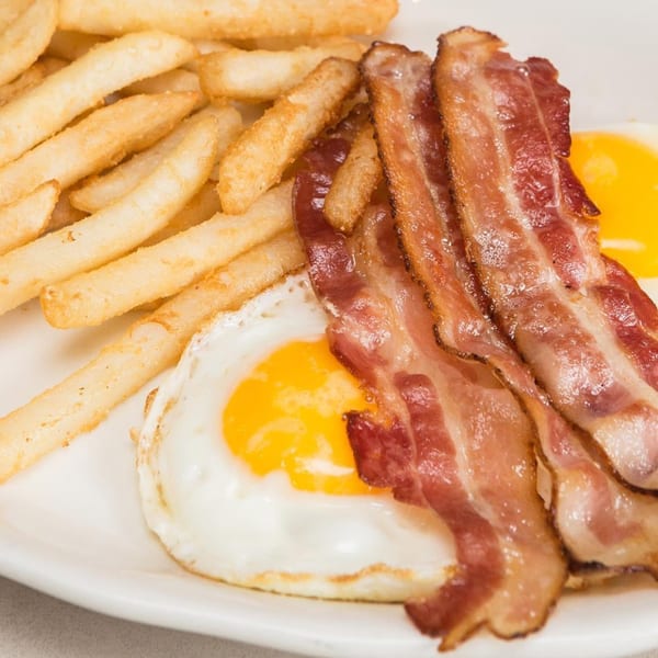A diner breakfast plate with crispy bacon, sunny-side-up eggs, and golden french fries.